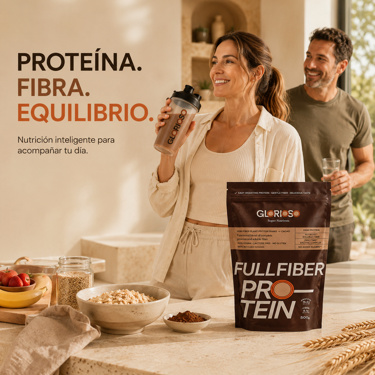 Mujer disfrutando de un batido Fullfiber Protein Glorioso en una cocina mediterránea luminosa, junto a proteína vegetal con fibra Nutriose®, cereales integrales, fruta fresca y cacao para una nutrición equilibrada y bienestar diario.