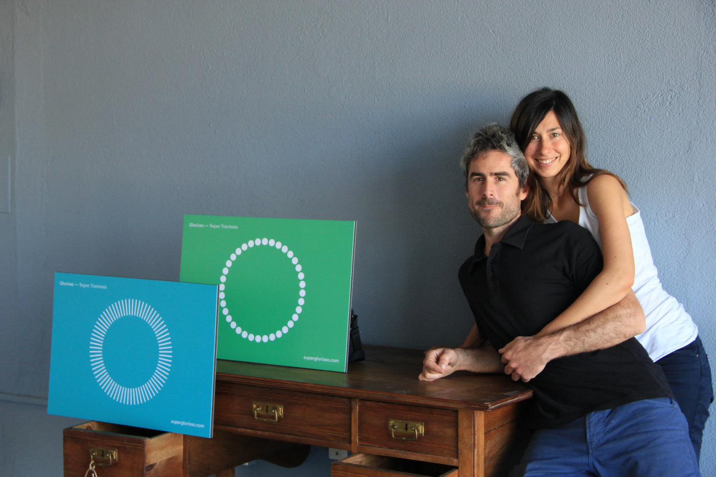 Pareja sonriente junto a escritorio de madera con carteles de colores que dicen 'Super Nutrientes'.