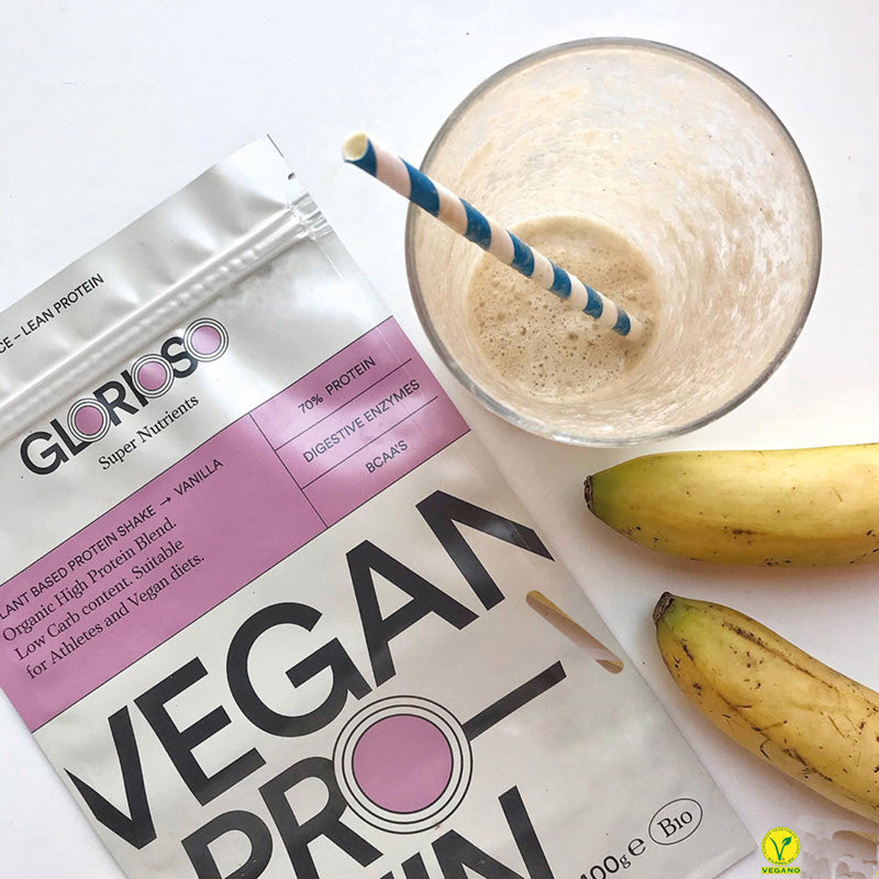 Proteína vegana sabor vainilla en polvo junto a plátanos y batido en vaso.