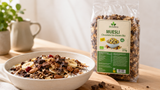 Bol de yogur con Biosfera Muesli Chocolate Sin Gluten Bio, plátano, frutos rojos, semillas y bolsa transparente de 375 g al fondo.