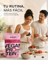 Envase de Proteína Vegana Fresa de Glorioso junto a una pareja en una cocina luminosa, con batido de fresa y desayuno saludable.